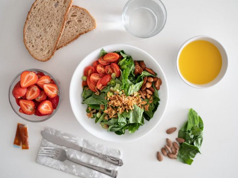Top view of a healthy salad and fresh ingredients with bread and juice on a white surface.