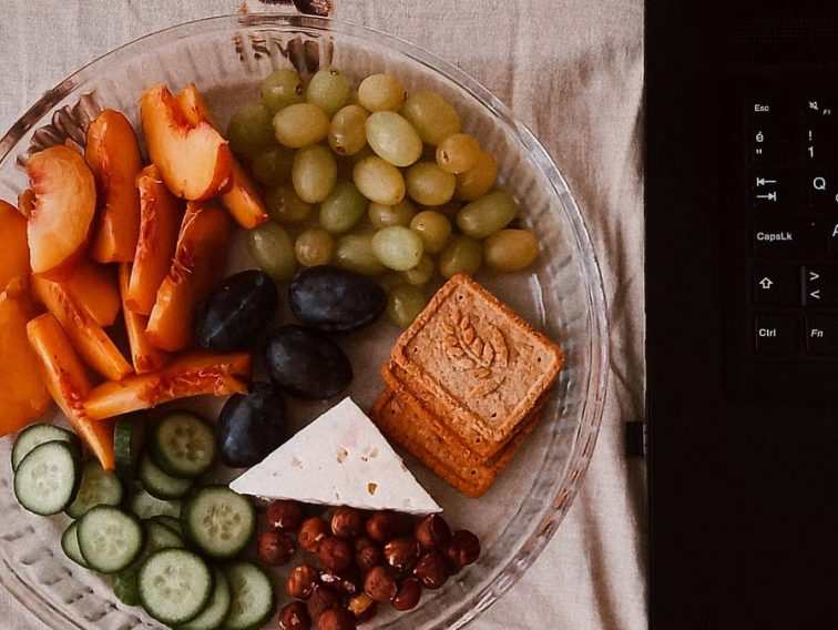 A delightful snack plate with fruits, cheese, and a laptop for a healthy lifestyle.