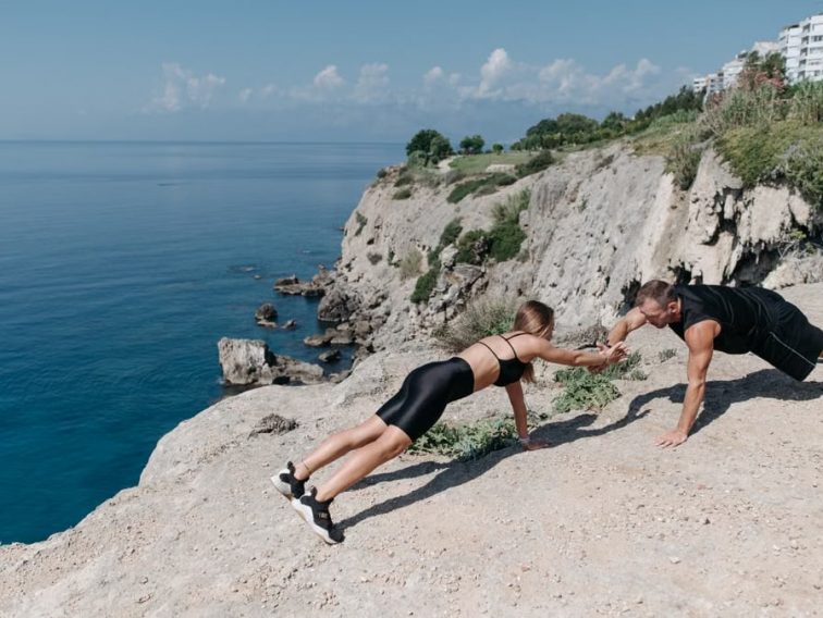 Fitness couple engaging in outdoor exercise on scenic seaside cliffs, promoting active lifestyle.